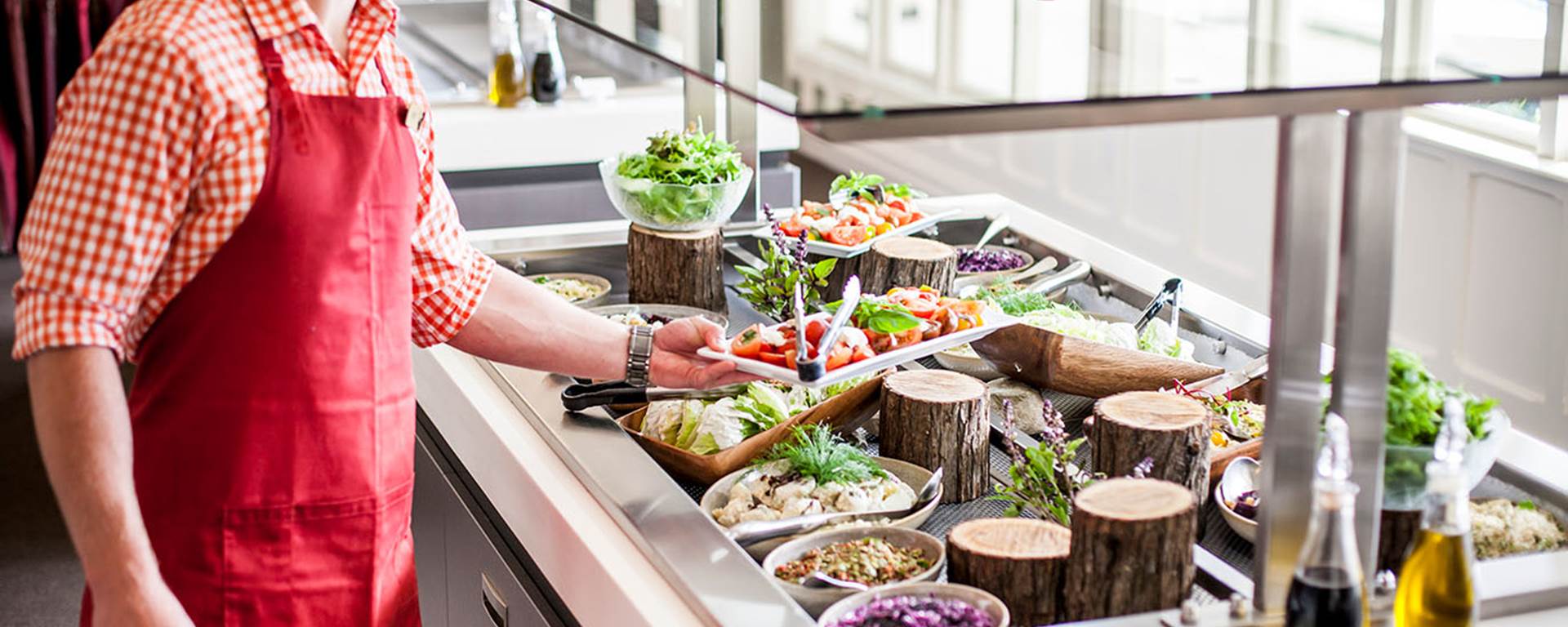 A server presents a selection of fresh salads and vegetables as a buffet station