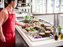A server presents a selection of fresh salads and vegetables as a buffet station