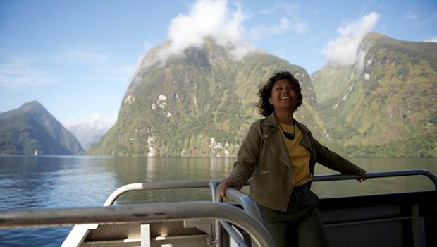A women leans on the edge of the vessel with a view of Doubtful Sound in the background 