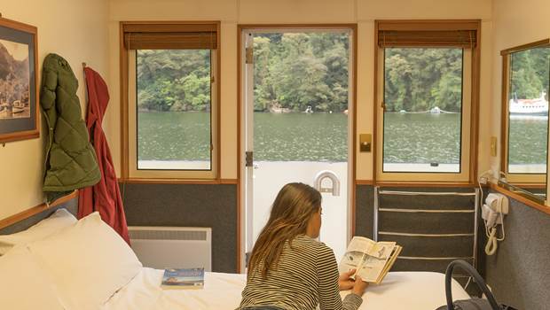 Woman on Overnight Cruise reads on bed in cabin with view of Doubtful Sound