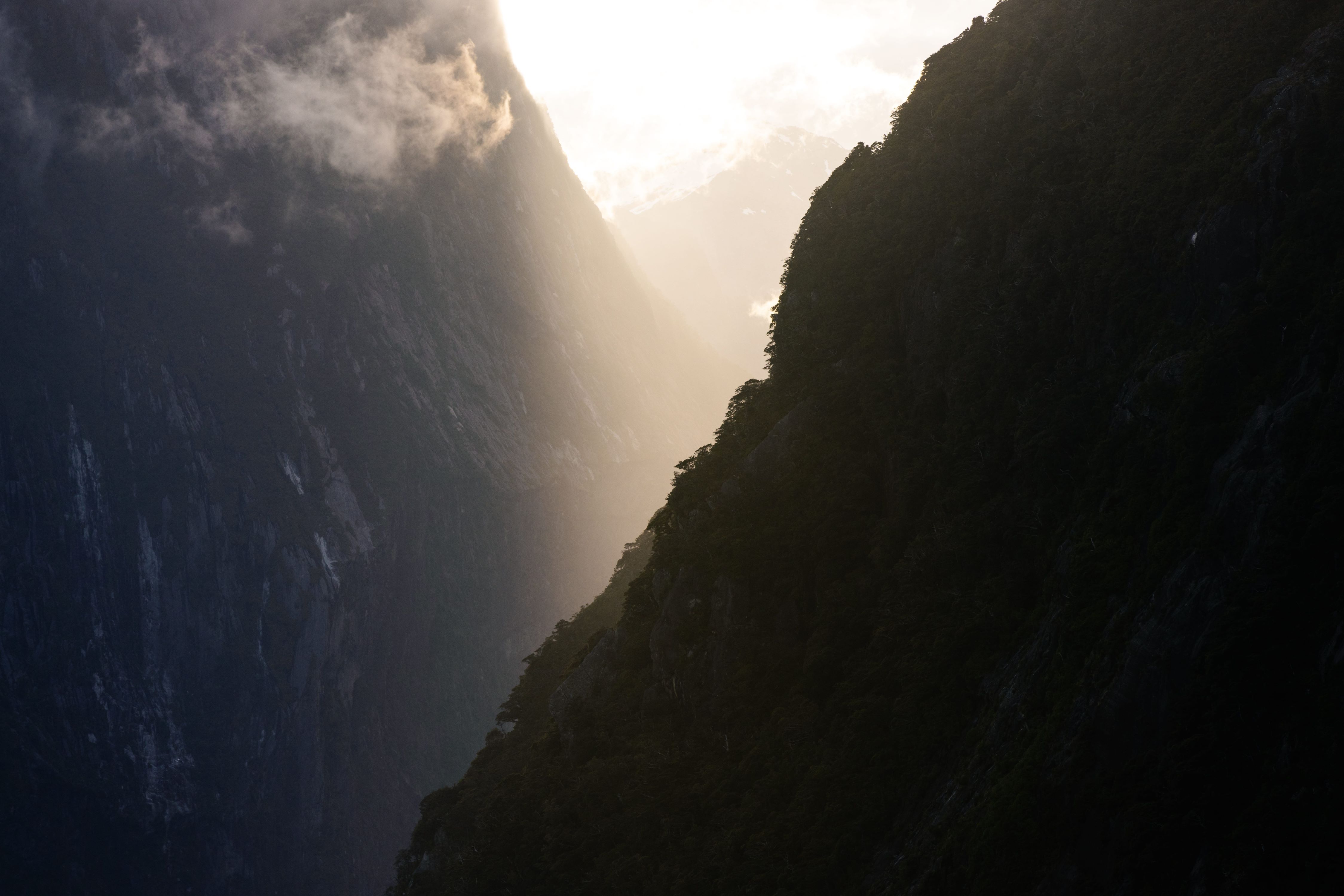 A shadowed morning view of the sun glaring between two mountains in Milford Sound