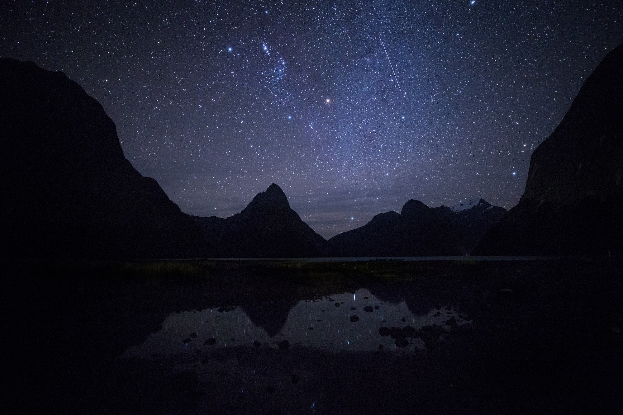 A dramatic starry night at Milford Sound, with the shadow of the mountains reflected in the water