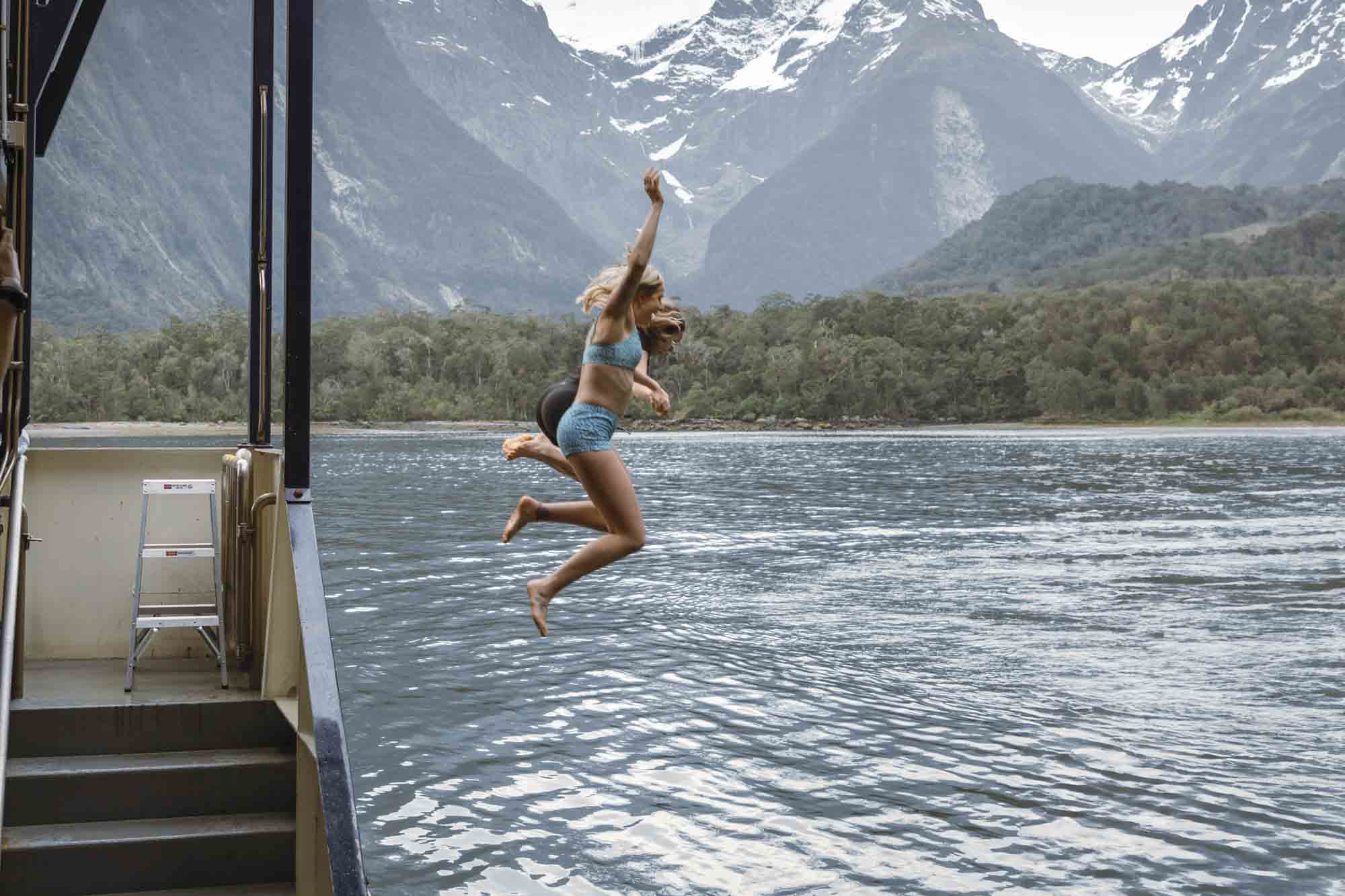 Two people jumping off the boat into Milford Sound