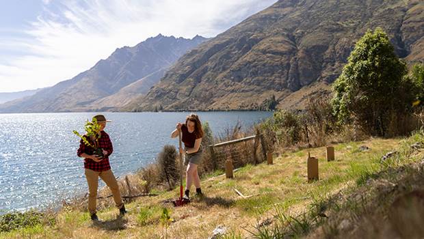Two women plant a tree at Walter Peak Farm Station, with Lake Wakatipu in the background