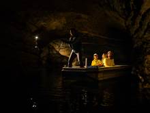 A group of three are guided through an underground cave on a small boat 