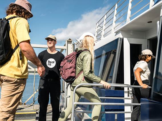Three guests are welcomed on board a ferry by a friendly RealNZ employee